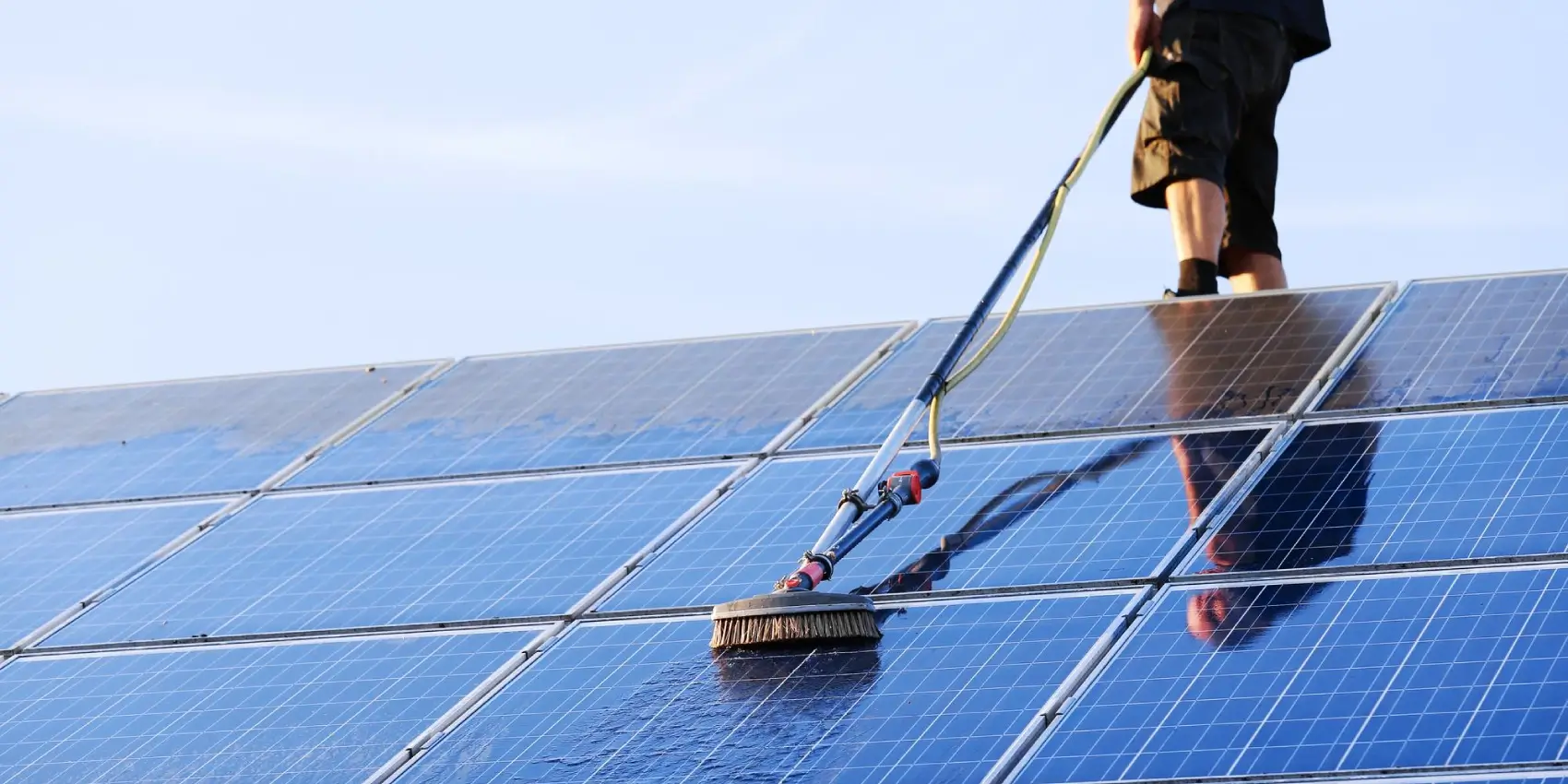A technician in uniform cleaning solar panels on a sunny day.